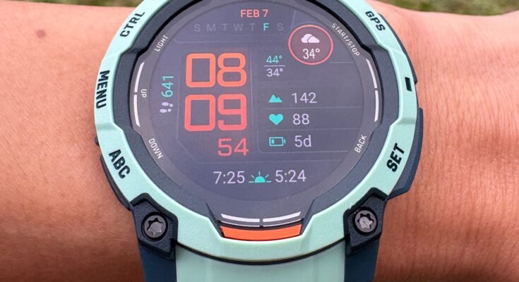 Vista aérea de una muñeca con un Garmin Instinct 3 Un rastreador de ejercicios en un reloj de brazalete con diseño turquesa y una gran pantalla digital