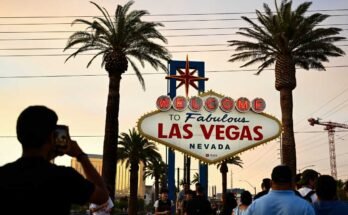 La gente toma fotos con la recepción del fabuloso panel de Las Vegas bajo un cielo naranja nebuloso mientras el sol se pone el 29 de julio de 2023.